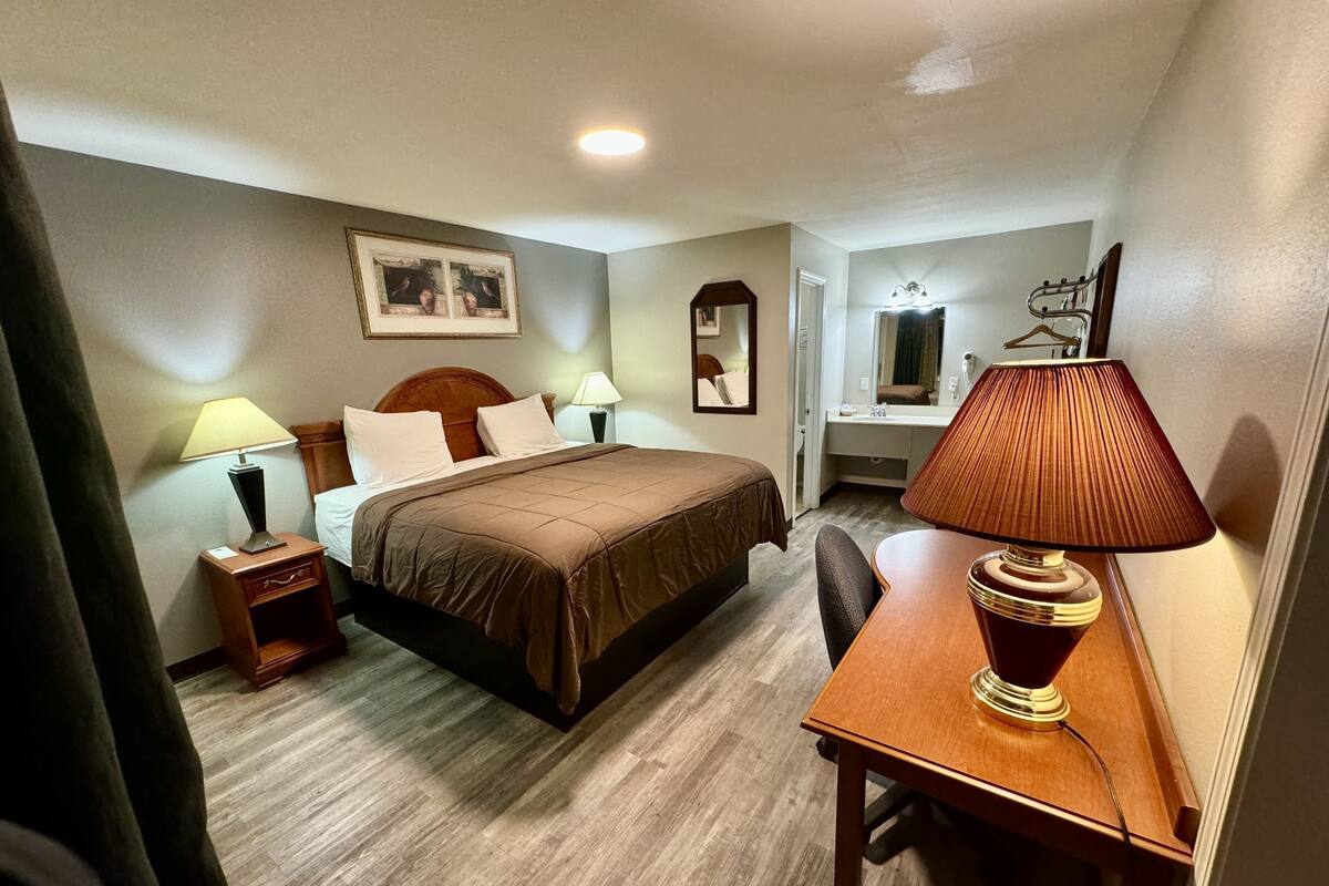 A hotel room with a bed, bedside tables, a desk, a chair, a mirror, and a lamp.