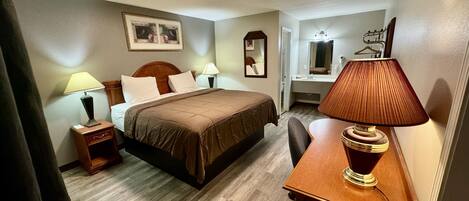 A hotel room with a bed, bedside tables, a desk, a chair, a mirror, and a lamp.