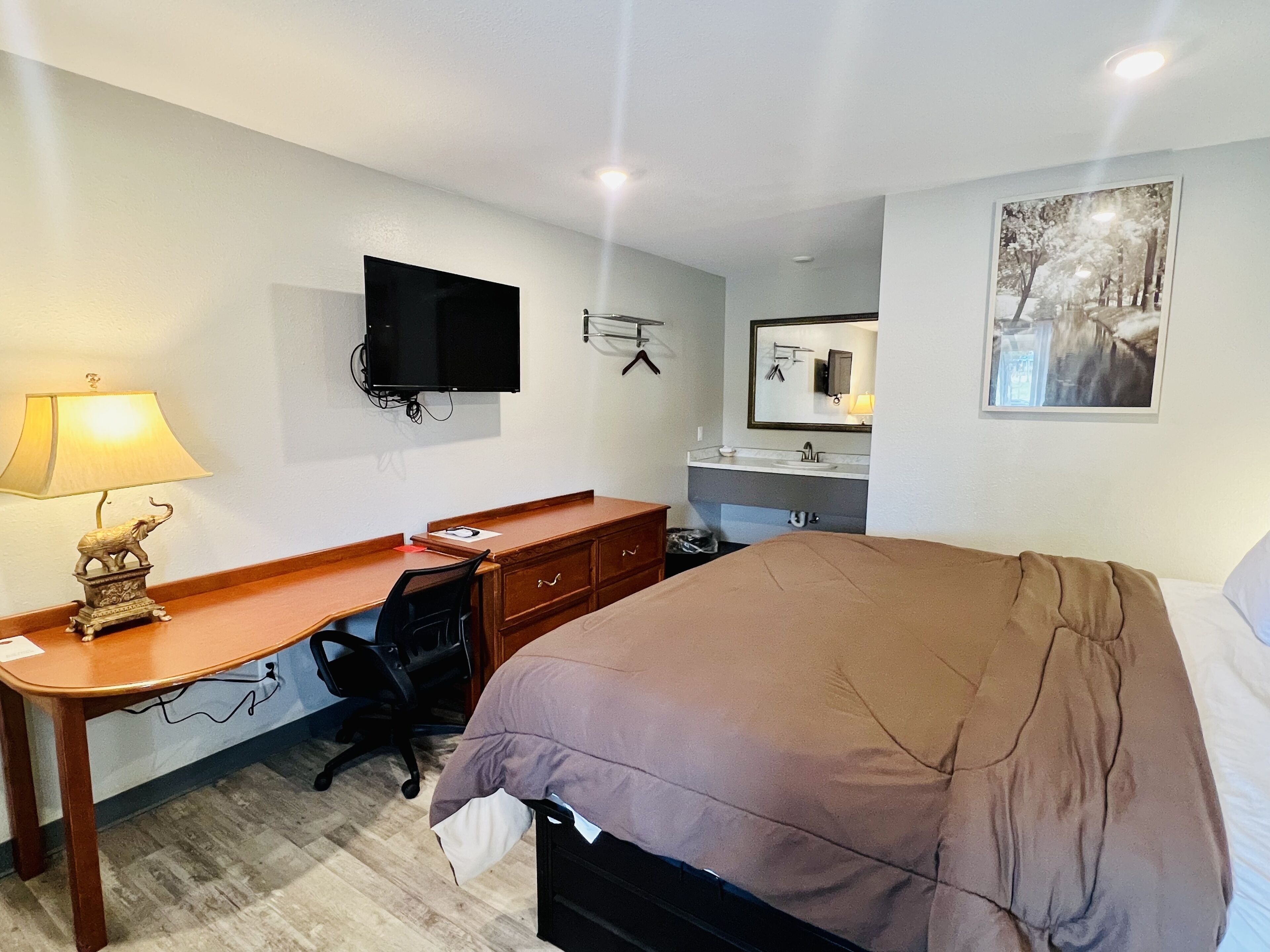 A hotel room with a bed, desk, chair, TV, and a bathroom with a mirror and sink.