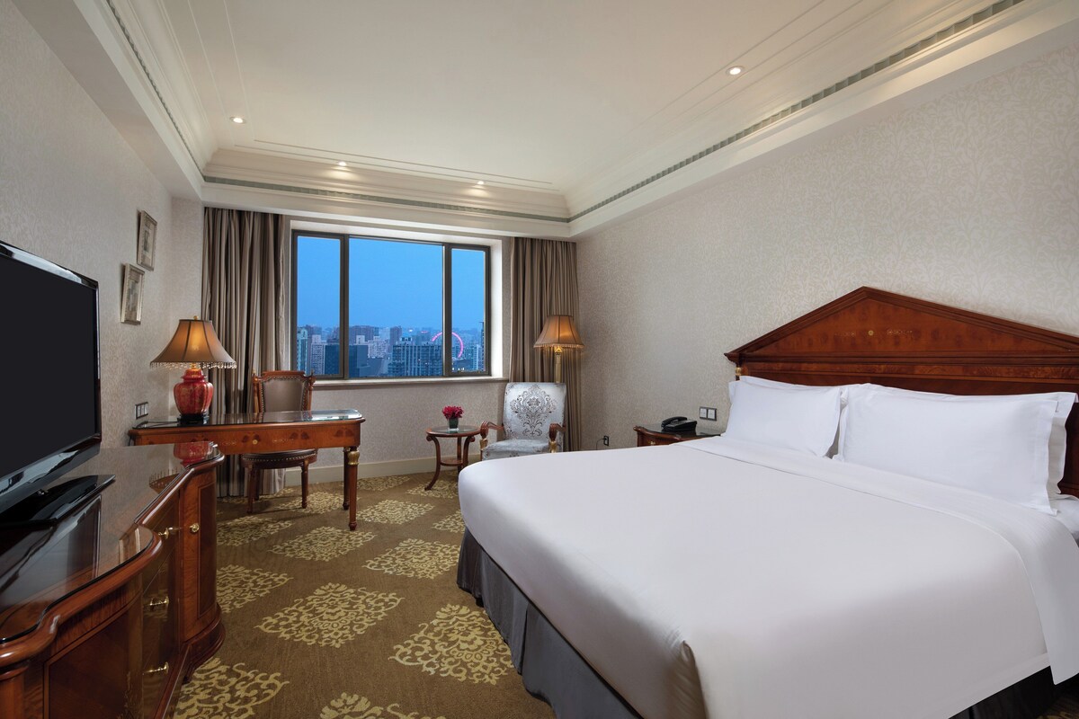 Une chambre d’hôtel avec un grand lit, un bureau, une chaise, une télévision et une vue sur la ville par la fenêtre.