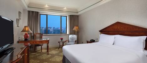 Habitación de hotel con una cama grande, un escritorio, un televisor y vistas a la ciudad a través de la ventana.