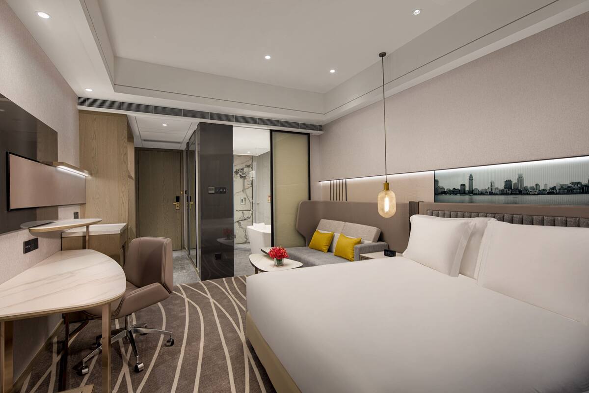 Una habitación de hotel moderna con una cama grande, un escritorio, una silla y una pintura de un paisaje urbano en la pared.