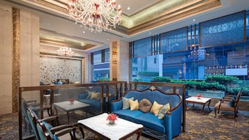 A spacious lobby with a blue sofa, wooden chairs, a marble coffee table, and a large chandelier.