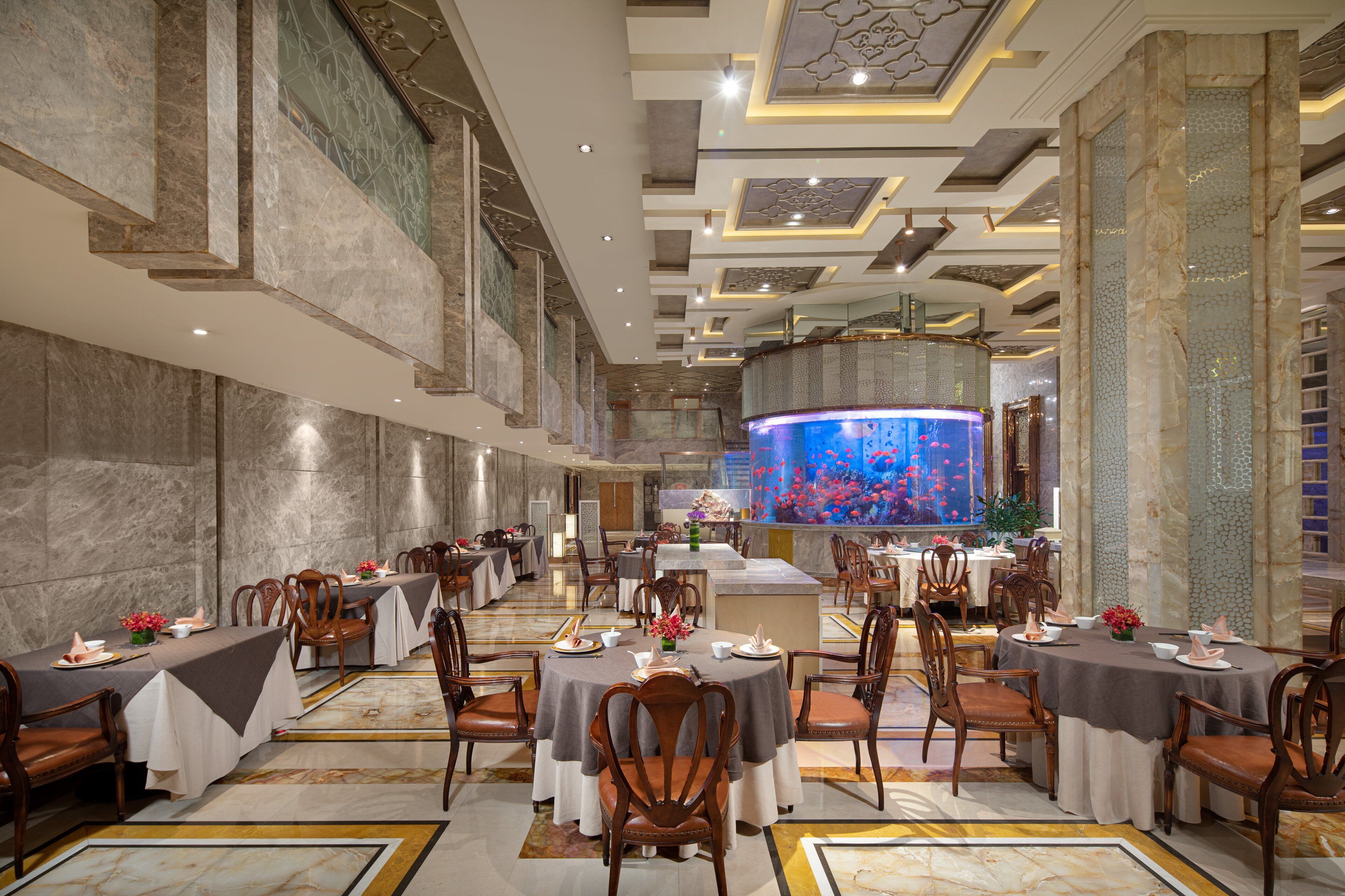 A spacious dining area with multiple round tables, chairs, and a large aquarium display.