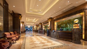 Een hotel lobby met een zwart-wit schachbordvloer, een receptiebalie en een muurschildering.