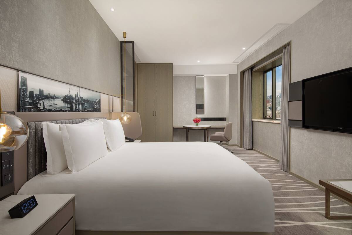 Una habitación de hotel moderna con una cama grande, un escritorio, un televisor y un cuadro con vistas a la ciudad.