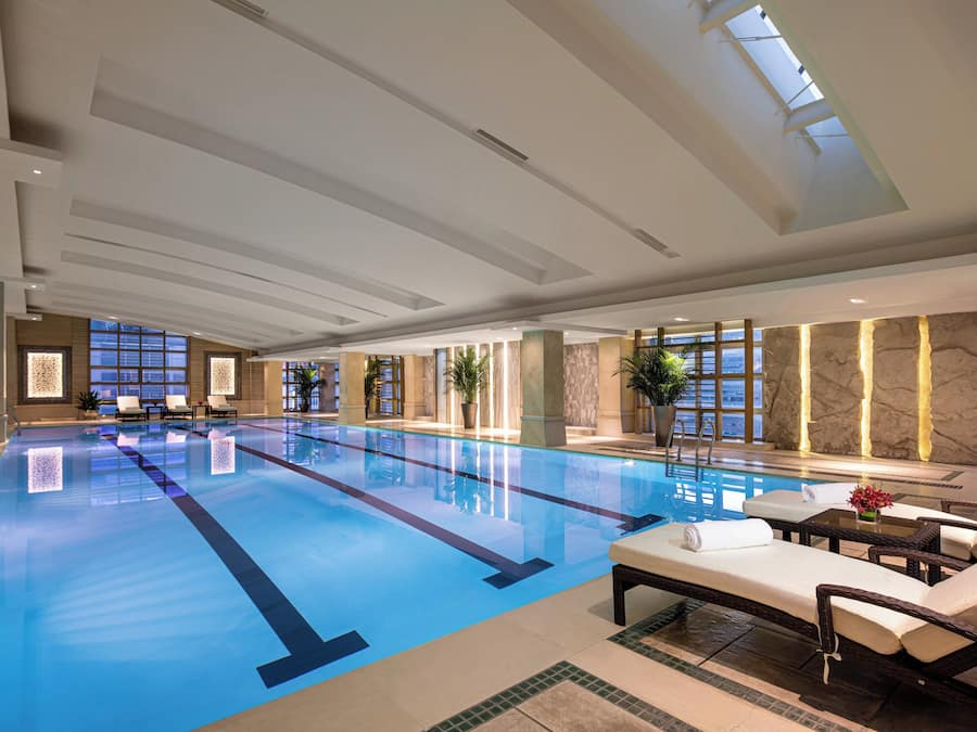 Una amplia piscina cubierta con agua cristalina y de color azul, rodeada de sillones de descanso y una zona de estar con una mesa.