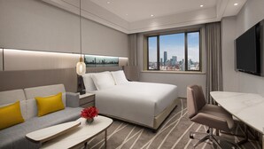 Een moderne hotelkamer met een bed, bank, bureau en uitzicht op de stad.