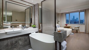 Een moderne badkamer met een groot bad, een wastafel met spiegel en een stadszicht door grote ramen.