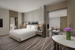 Una habitación de hotel moderna con una cama grande, mesitas de noche, una mesa redonda con un florero y un espejo grande.