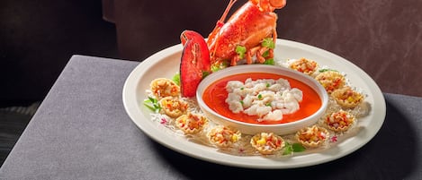 Un homard présenté sur une assiette, accompagné d’un bol de soupe et de quelques amuse-gueule.