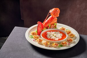 A lobster on a plate with a bowl of soup and small appetizers.
