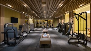 Ein Fitnessraum mit verschiedenen Trainingsgeräten, einer zentralen Bank und einem Fernseher an der Wand.