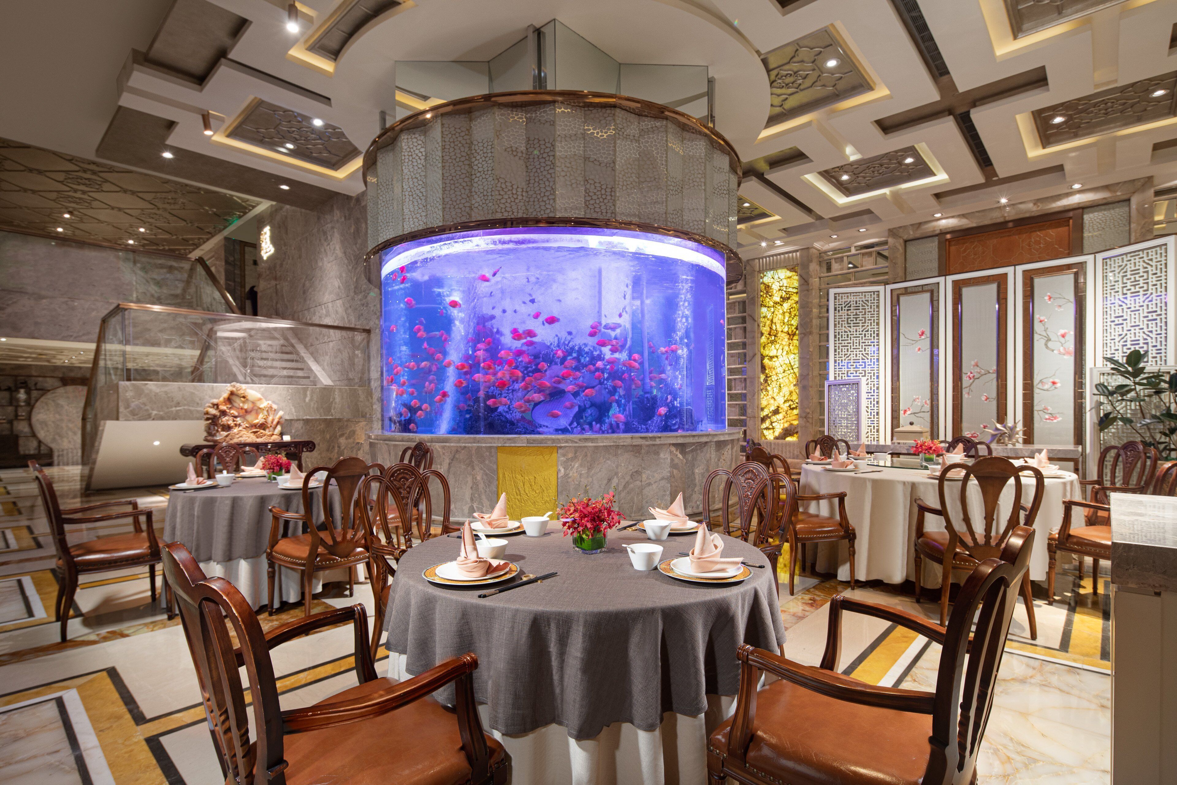 A dining area with round tables, chairs, and a large aquarium.