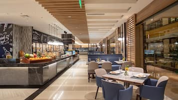 A modern hotel lobby with a central bar area, seating arrangements, and a glass-enclosed dining area.