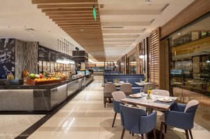 A modern hotel lobby with a central bar area, seating arrangements, and a glass-enclosed dining area.