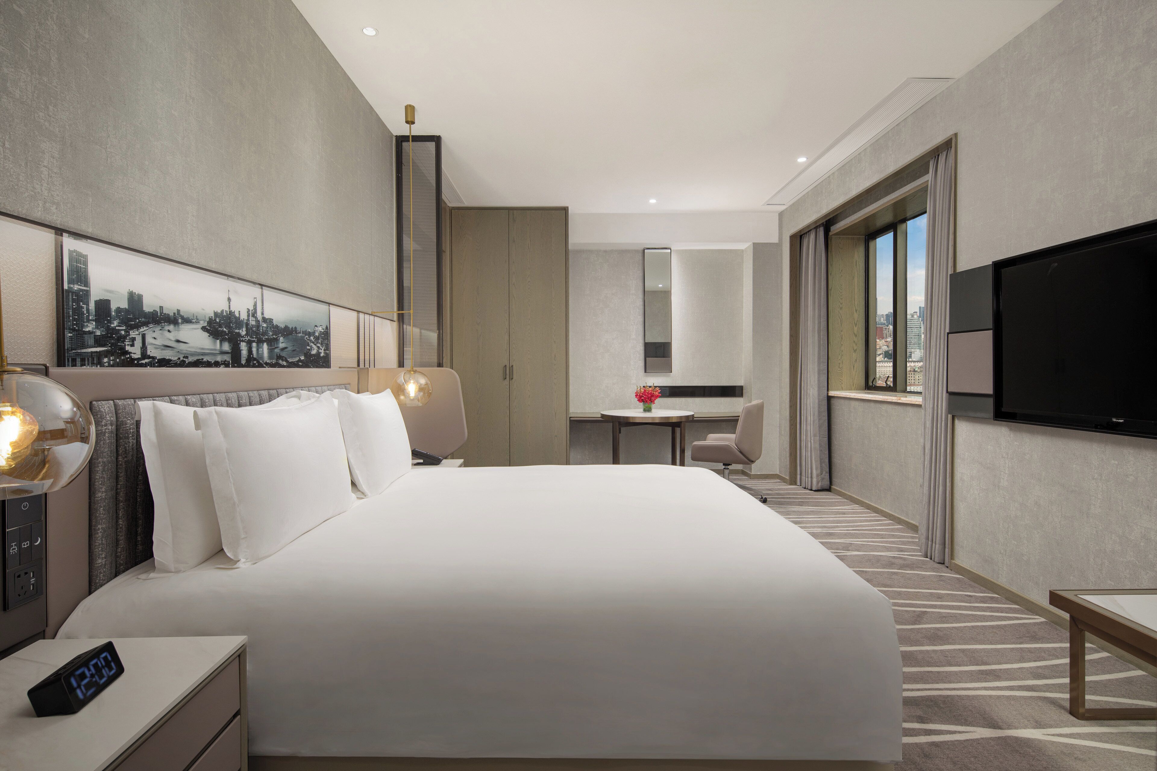 A hotel room with a large bed, a desk, a television, and a cityscape view.