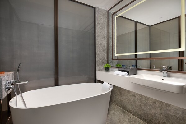 A modern bathroom with a freestanding bathtub, a large mirror, and a countertop with a sink and toiletries.