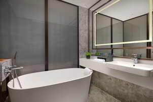 A modern bathroom with a freestanding bathtub, a large mirror, and a countertop with a sink and toiletries.