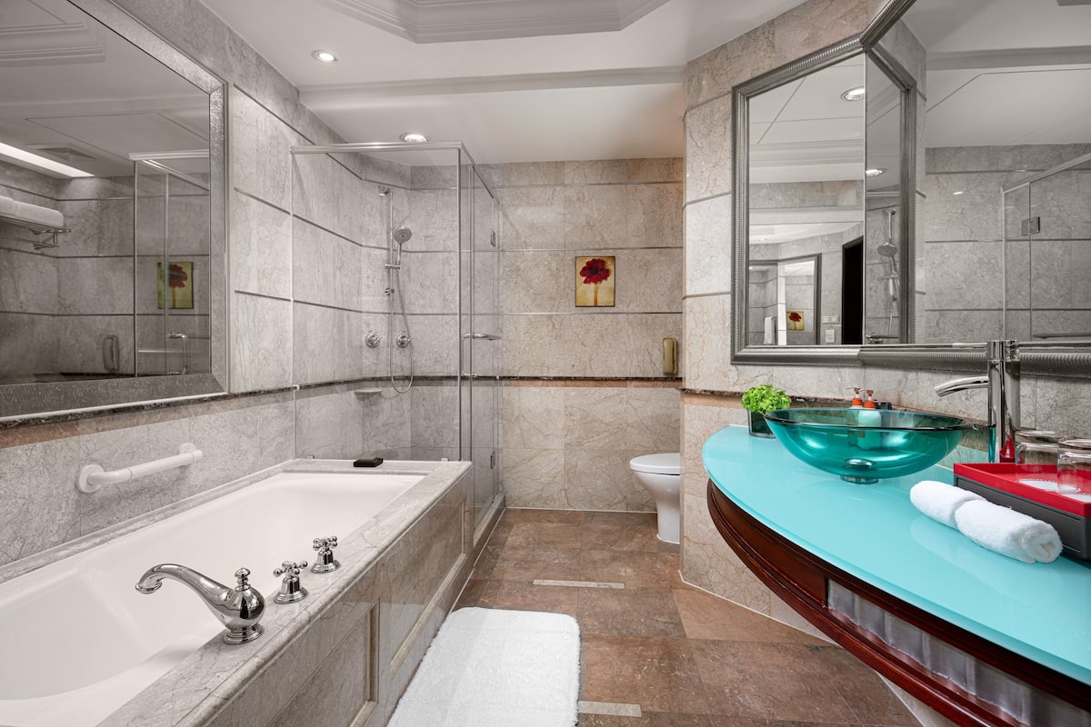 Un baño moderno con ducha envuelta en vidrio, una bañera amplia y un tocador con lavabo de cristal.