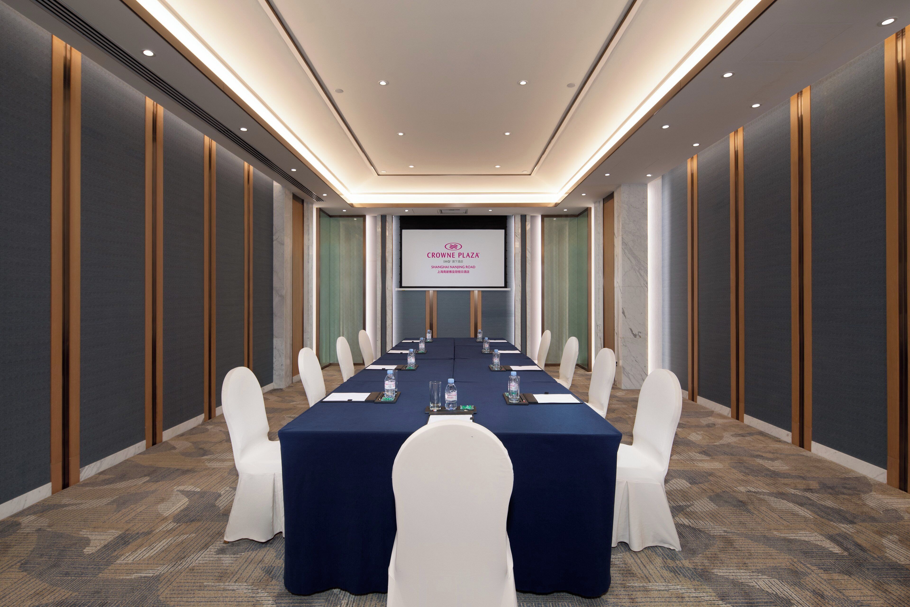 A conference room with a long table, white chairs, and a presentation screen.