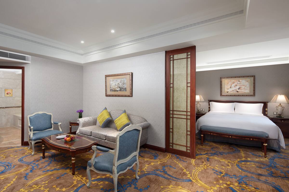 Habitación de hotel con cama, sofá, sillón, mesita de centro y alfombra de diseño geométrico.