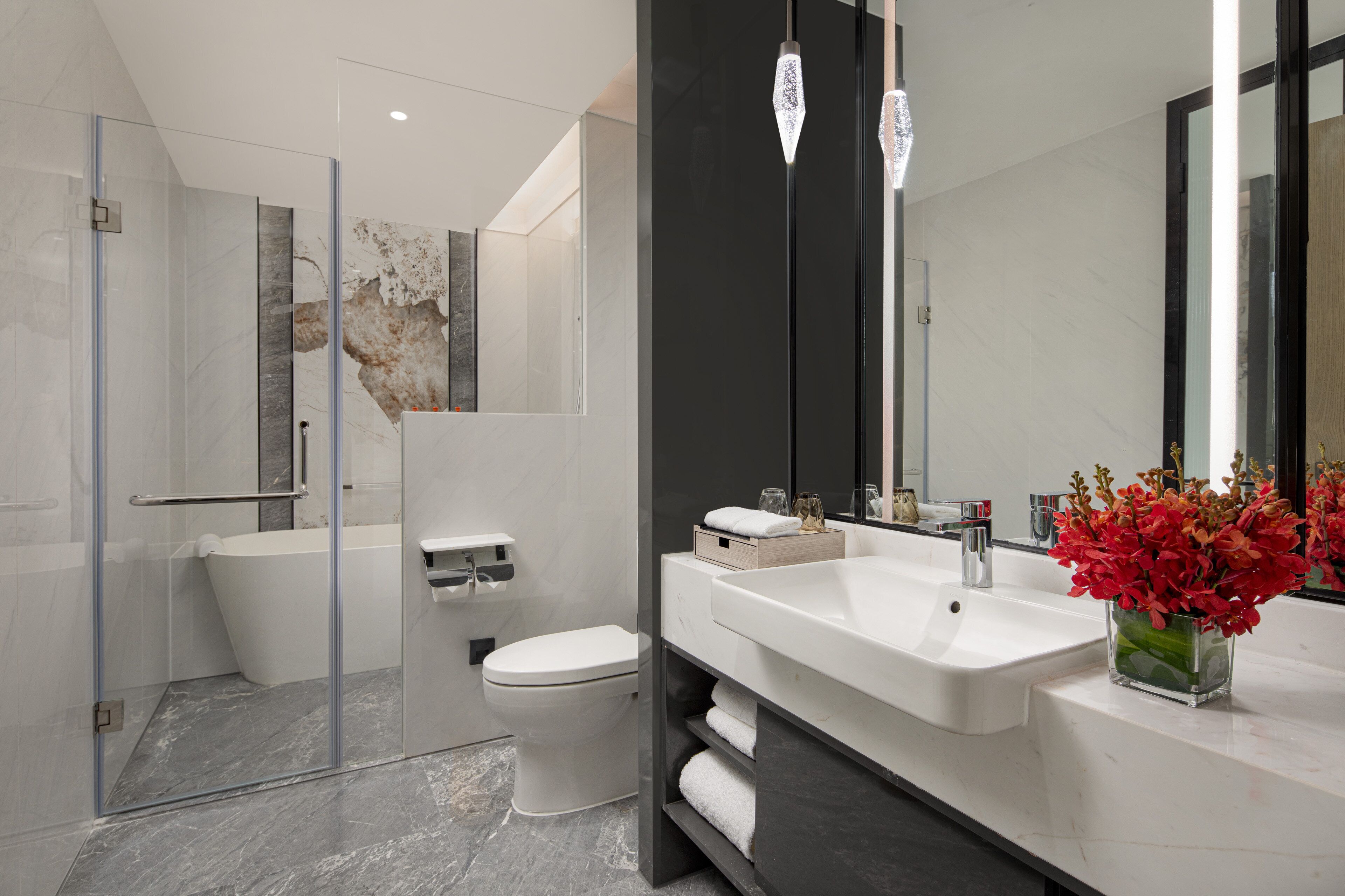 Et moderne badeværelse med en glas brusekabine, et hvidt toilet, en stor hvid vask og et spejl med mørk ramme.
