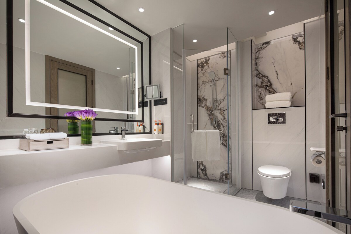 Une salle de bain moderne avec un grand miroir, une baignoire blanche, une douche à l’italienne et des murs en marbre.