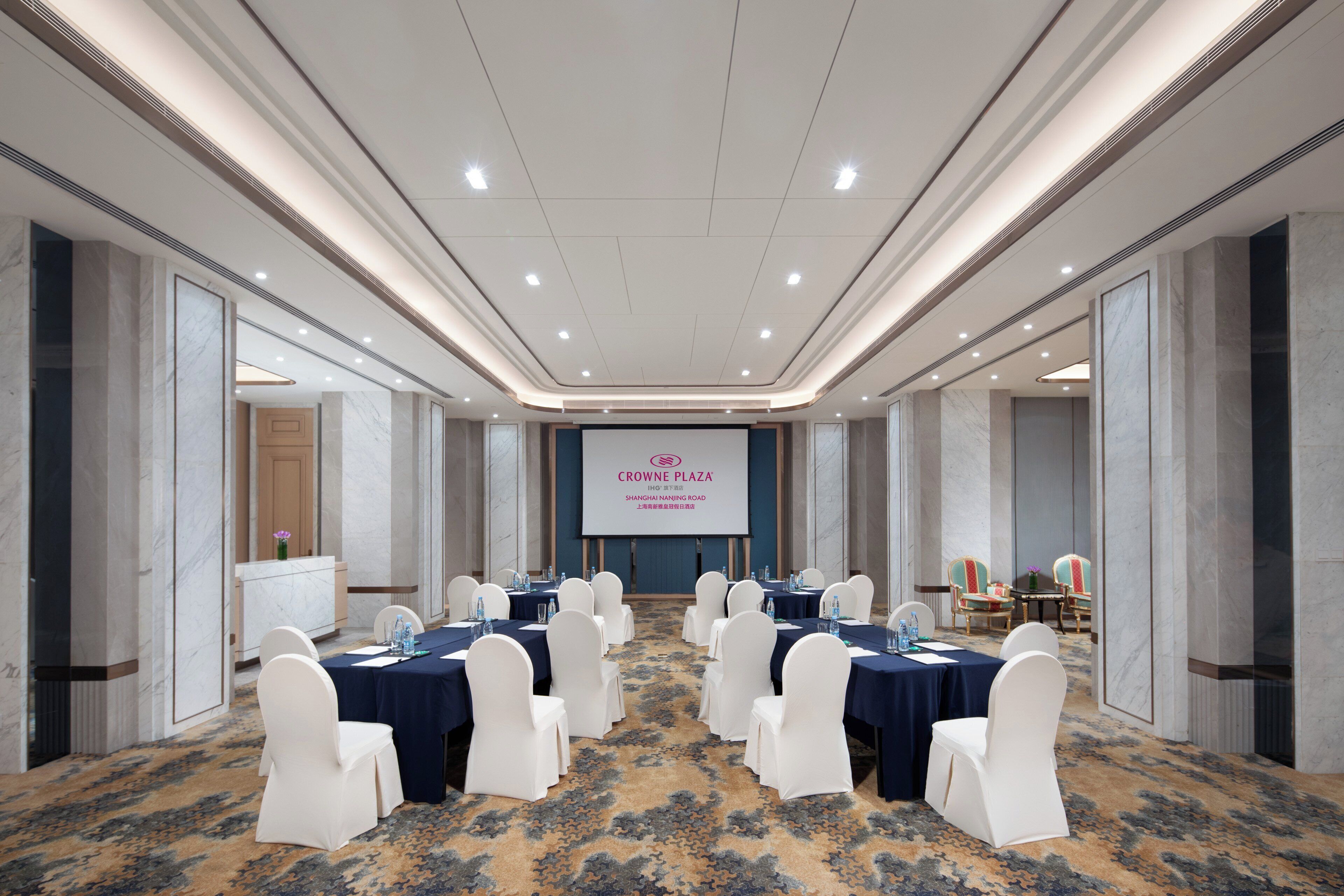 A conference room with a projector screen displaying 'CROWNE PLAZA' and 'SHANGHAI NING ROAD' text.