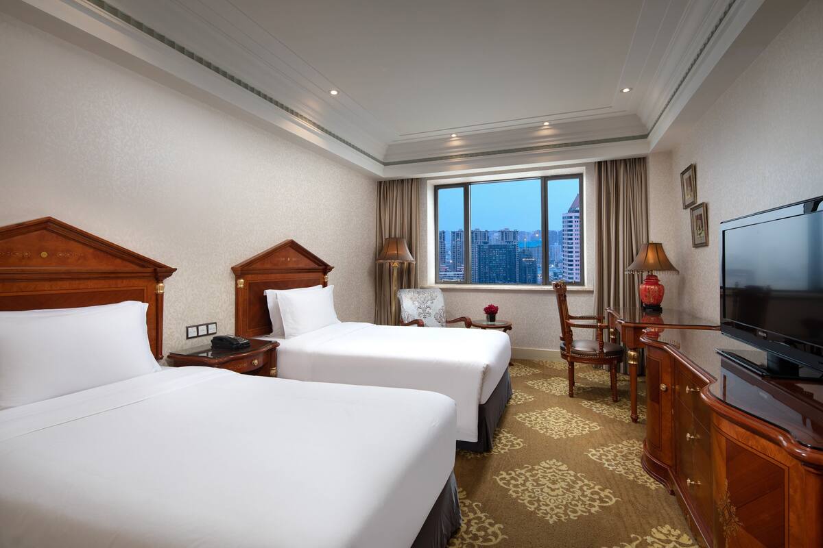 Habitación de hotel con dos camas, televisión, escritorio y ventana con vista a la ciudad.