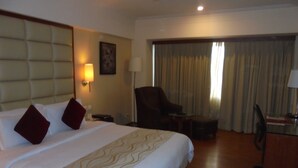 Una habitación de hotel con una cama grande, una silla, un escritorio y un ventanal con cortinas.