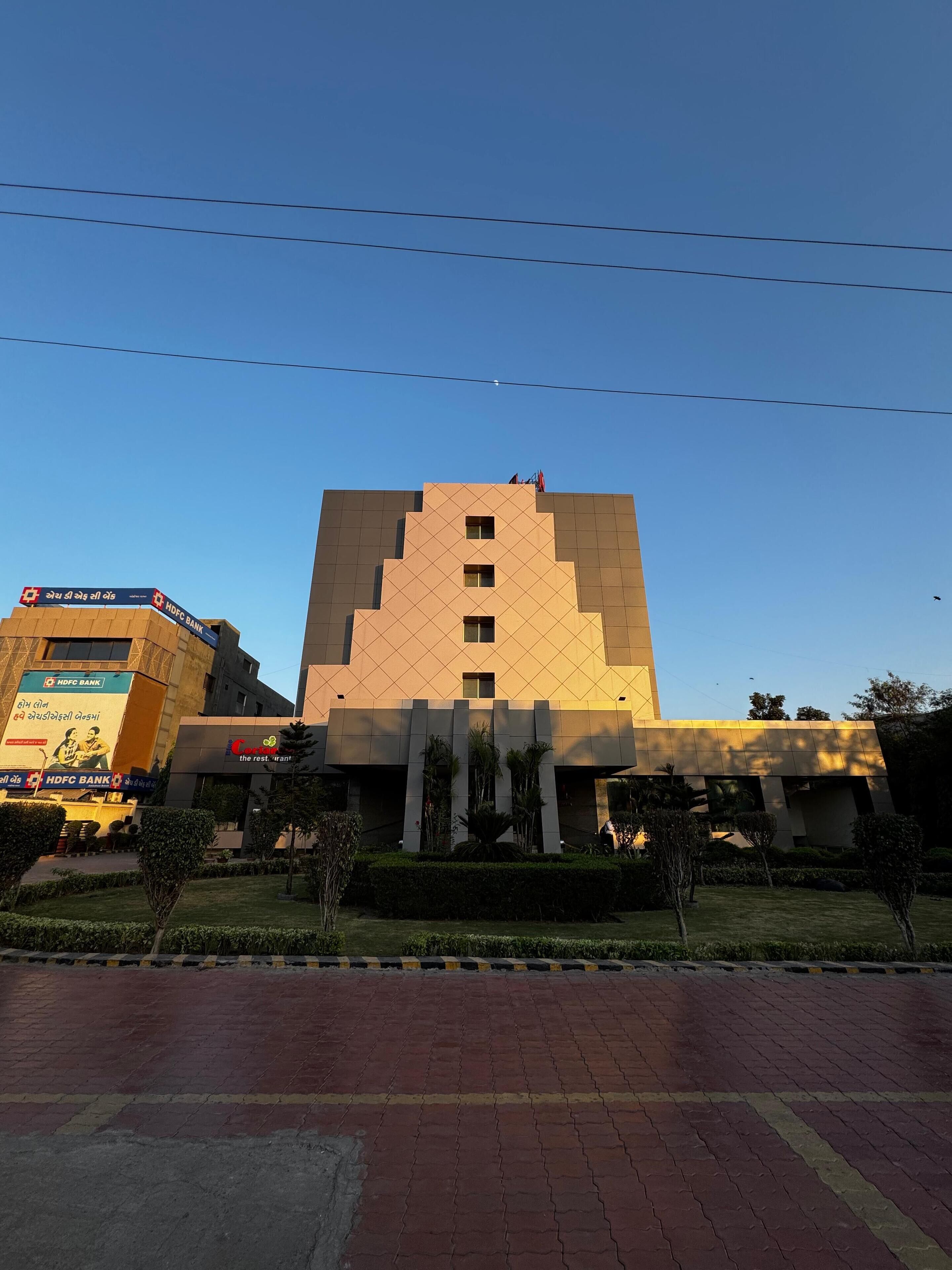Un edificio moderno con fachada geométrica, un jardín ajardinado en primer plano y un camino pavimentado.