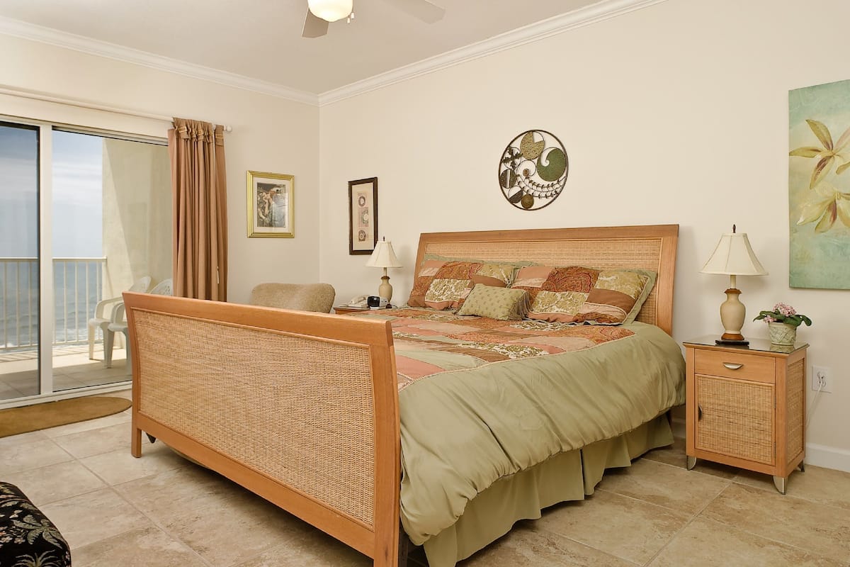 Un dormitorio con cama, mesita de noche, ventilador de techo y vista al océano.
