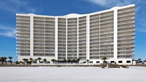 A large, multi-story hotel with numerous balconies, located on a beach with palm trees. - Admirals Quarters by Wyndham Vacation Rentals (Orange Beach)