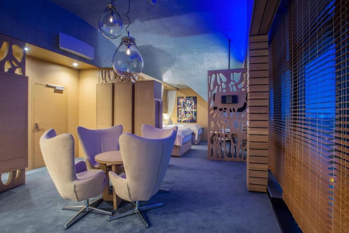 Una habitación de hotel moderna con una cama grande, una zona de estar con sillas y un diseño de pared original.
