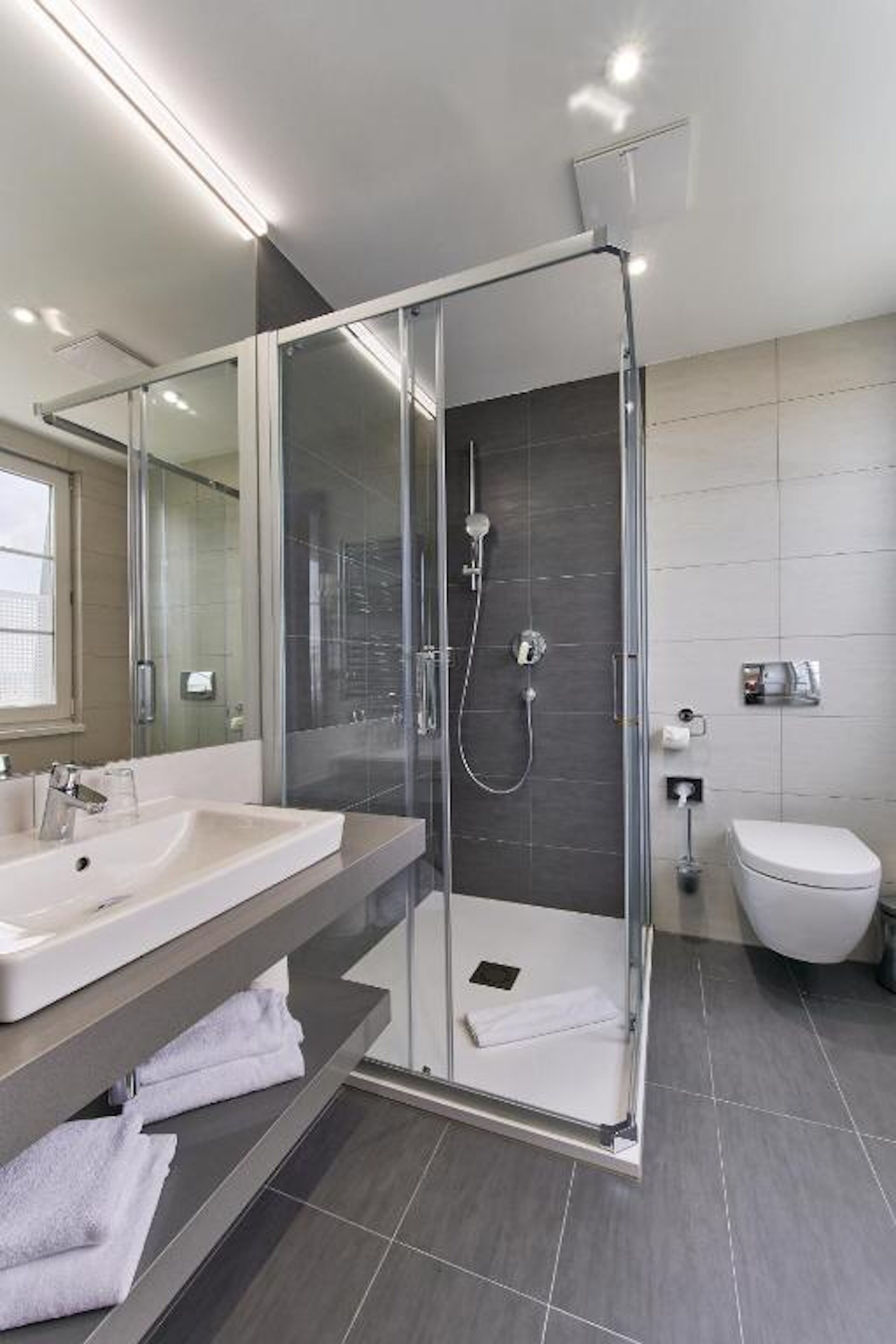 A modern bathroom with a glass-enclosed shower, a large mirror, and a white sink.