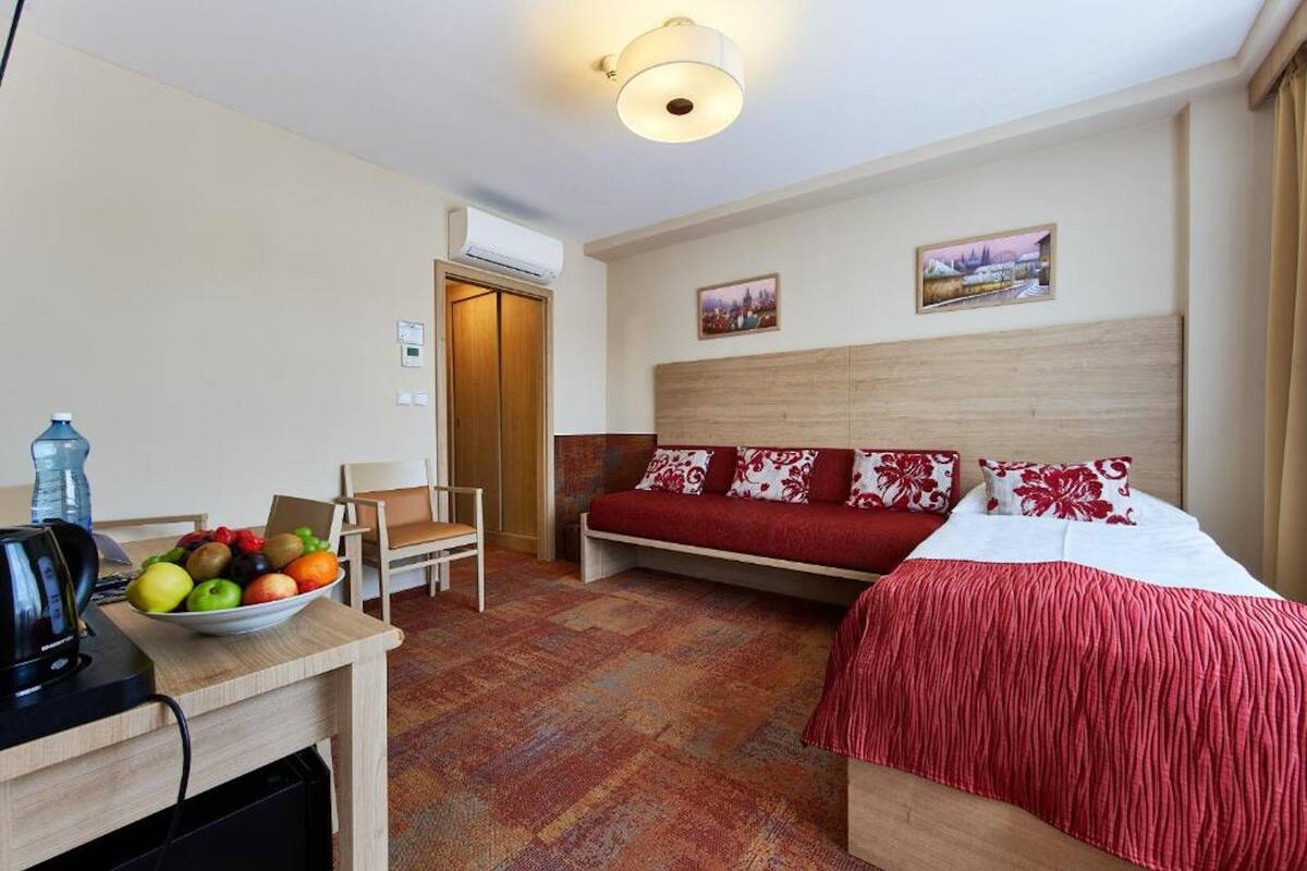 Habitación de hotel con cama, escritorio con tetera, una silla, frutero y aire acondicionado instalado en la pared.