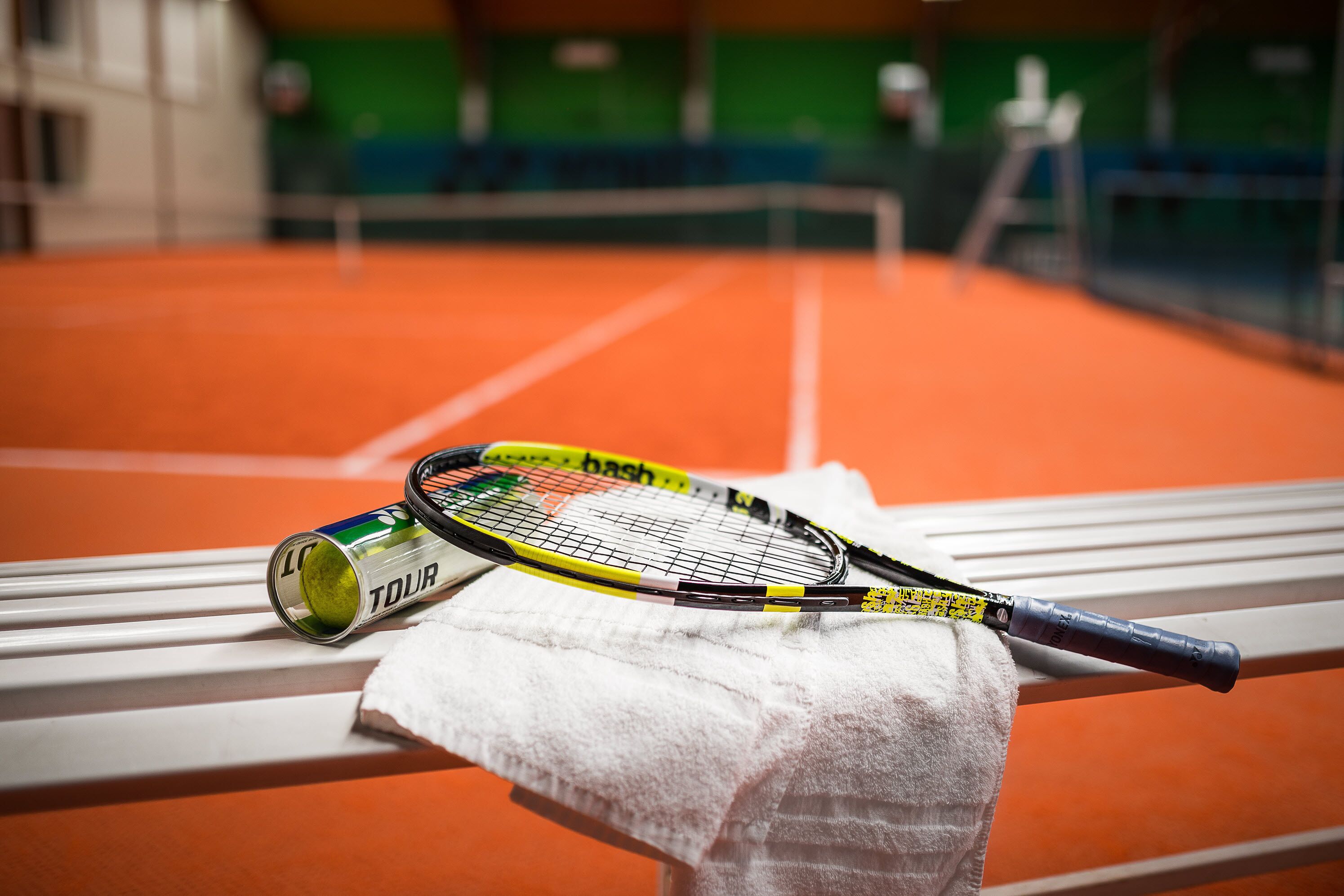 En tennisraket og en dåse tennisbolde på en bænk med et håndklæde.