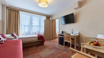 Habitación de hotel con cama, escritorio, silla, televisión y ventana con cortinas.