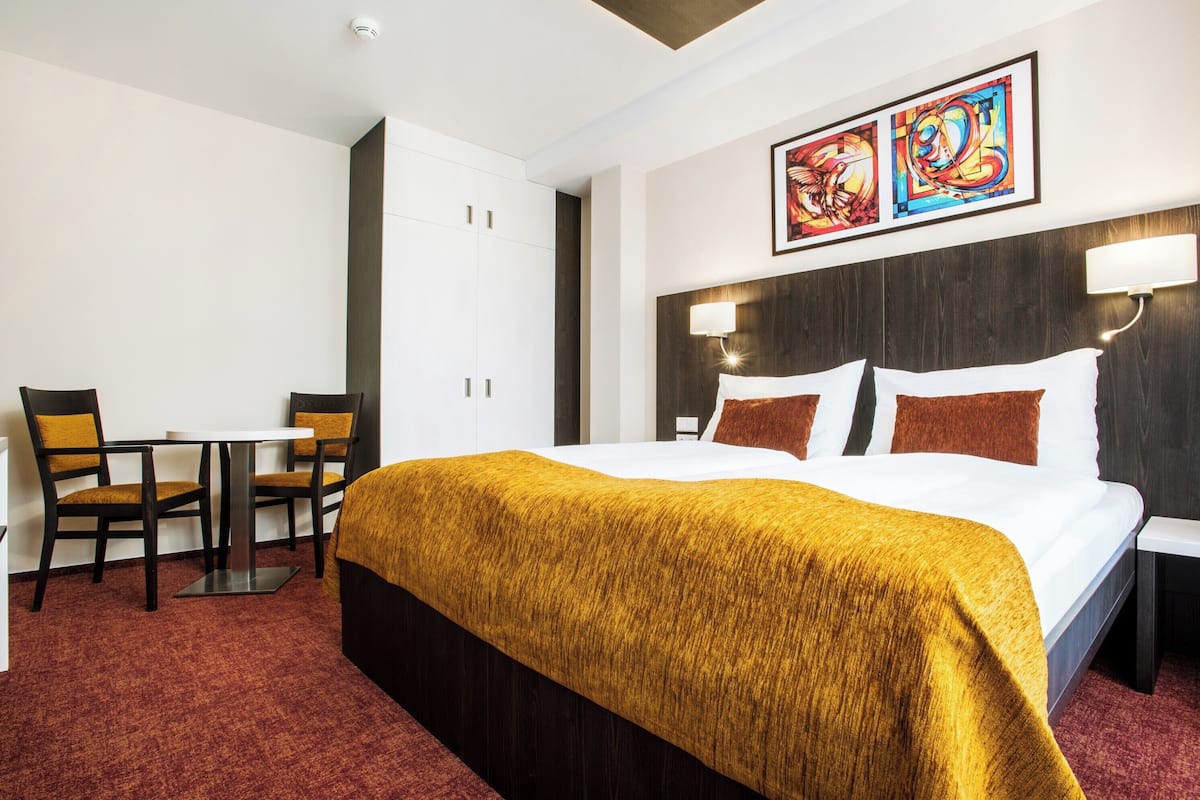 Habitación de hotel con una cama grande, un escritorio con dos sillas, una mesita y una obra de arte colgada en la pared.