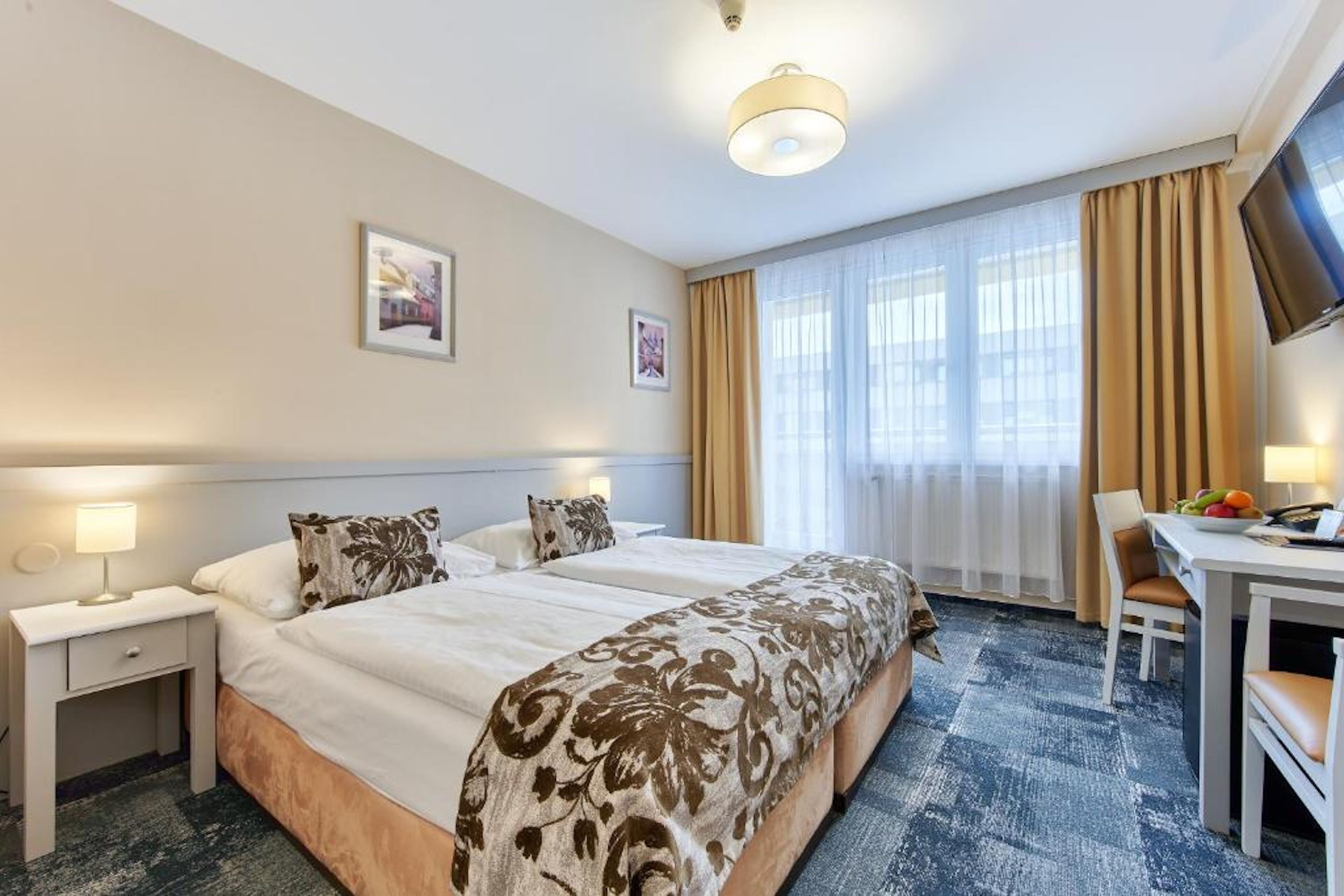 A hotel room with two beds, a desk with a chair, a television, and a window with curtains.