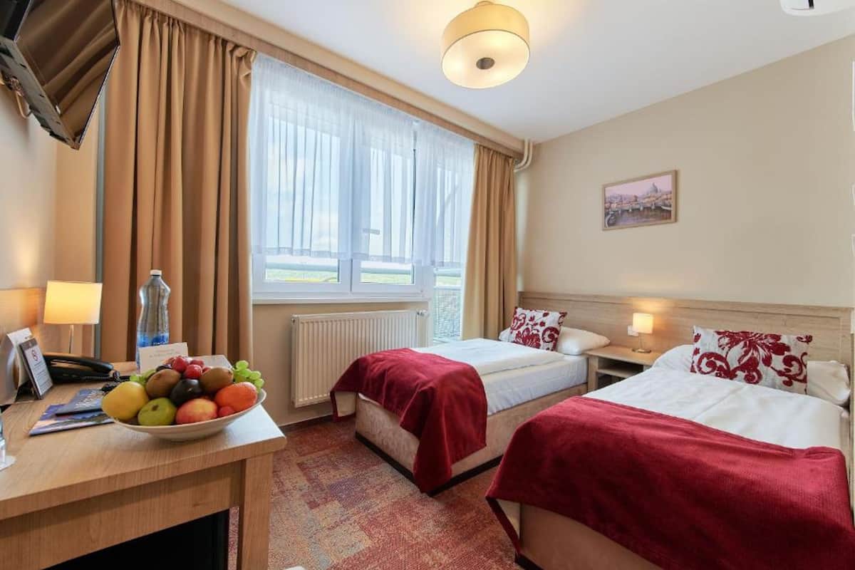Habitación de hotel con dos camas, un escritorio con frutero, una lámpara y una ventana con cortinas.