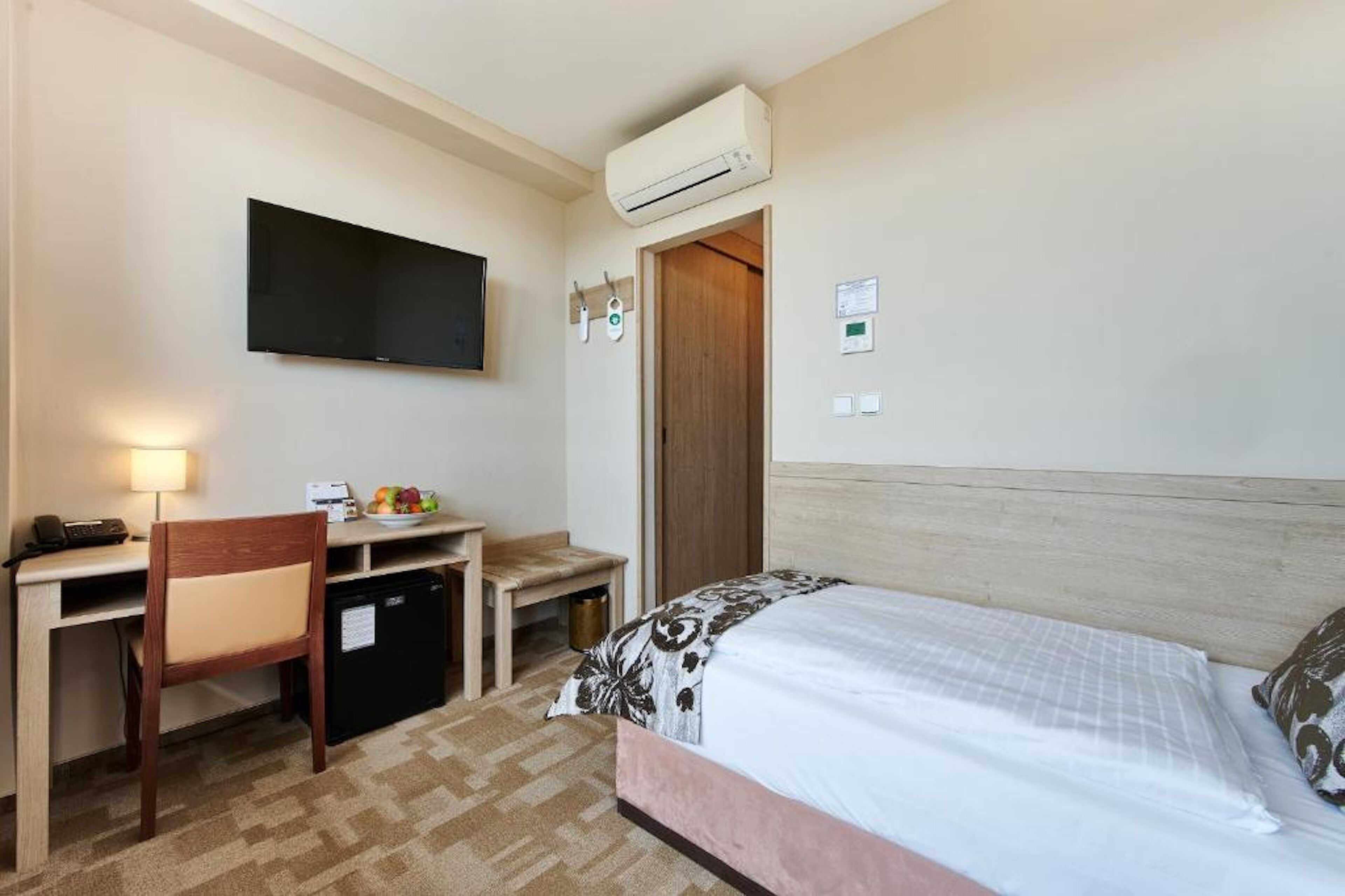 Habitació d'hotel amb llit, escriptori, cadira, televisió i una petita cuineta.