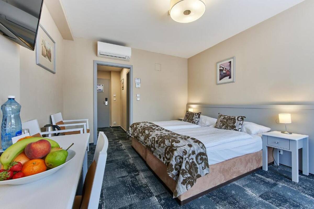 Habitación de hotel con cama, mesita de noche y frutero sobre un escritorio.