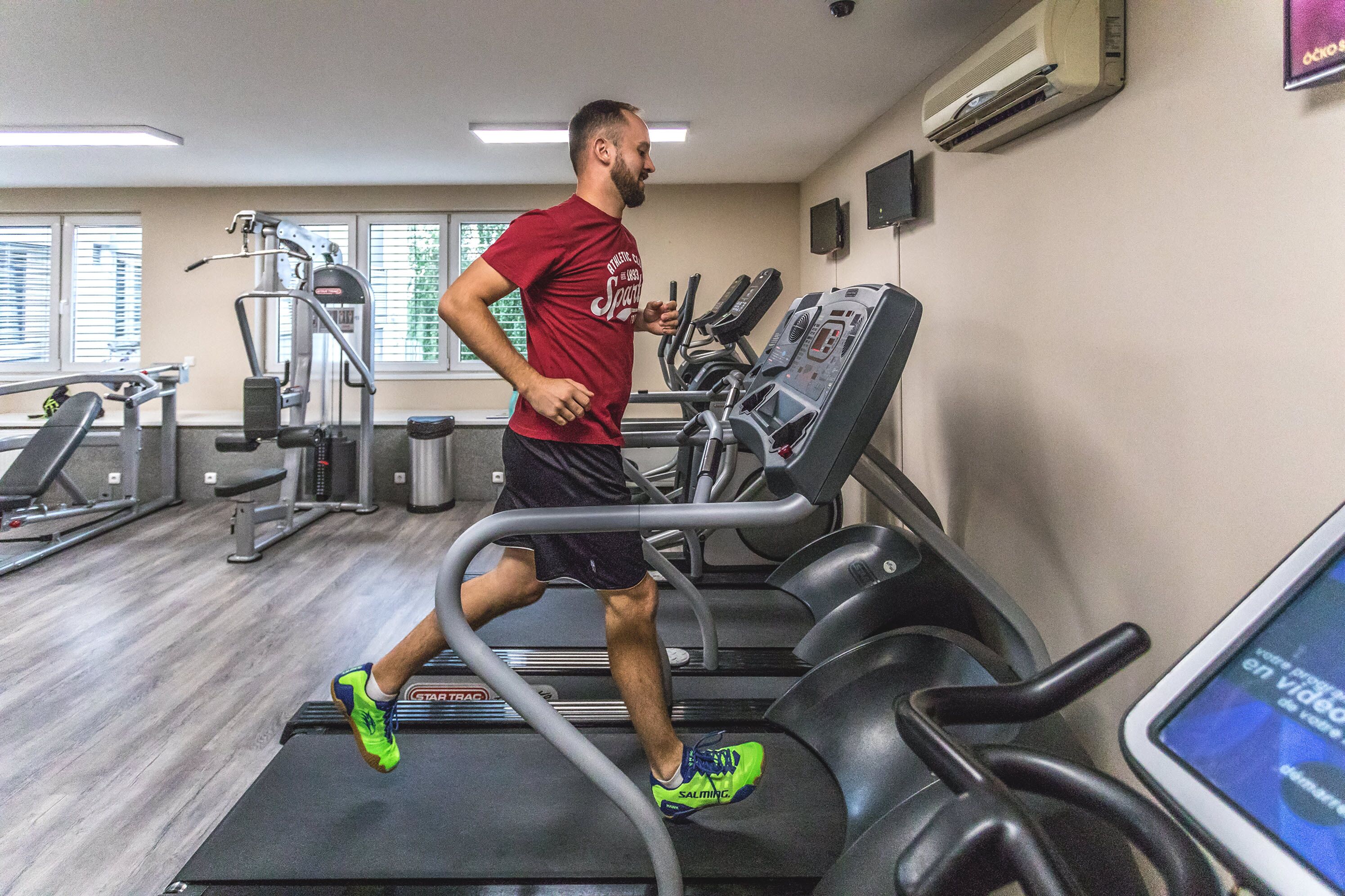 A gym with treadmills, weight machines, and a TV screen displaying a video.