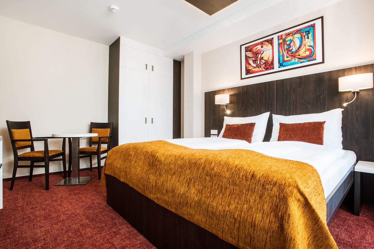 Habitación de hotel con una cama grande, un escritorio con dos sillas y obras de arte en la pared.
