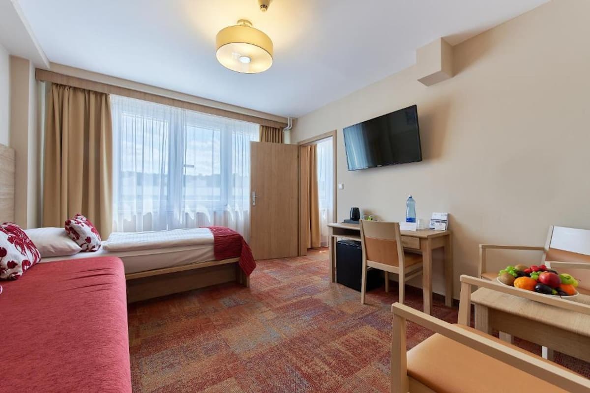 Habitación de hotel con cama, escritorio, silla, televisión y ventana con cortinas.
