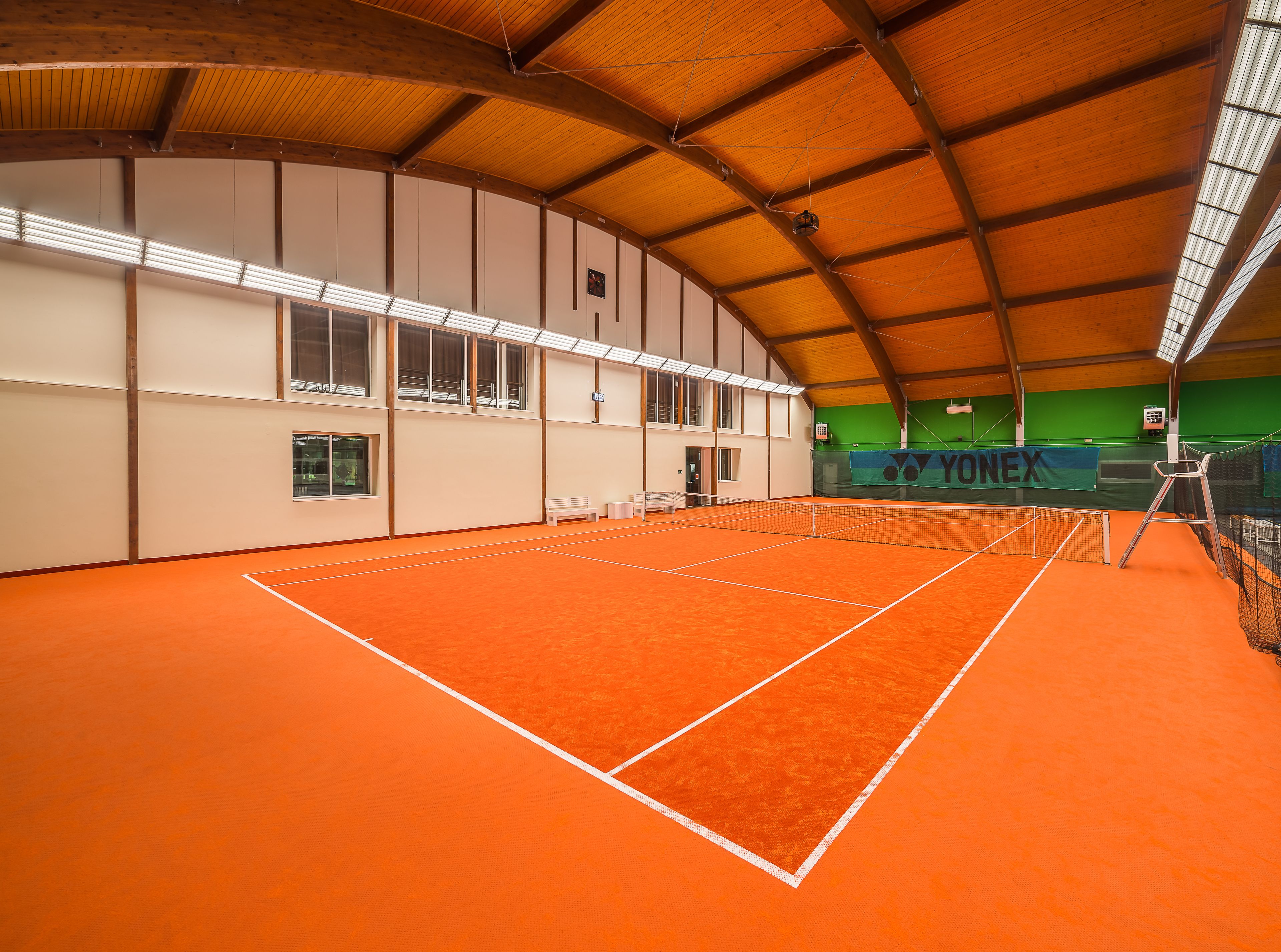 Una cancha de tenis interior con techo de madera y piso naranja.