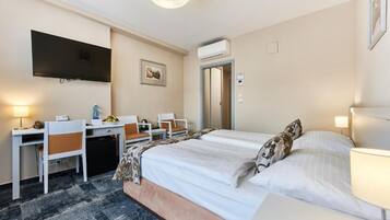 A hotel room with a bed, desk, chairs, a television, and an air conditioning unit.