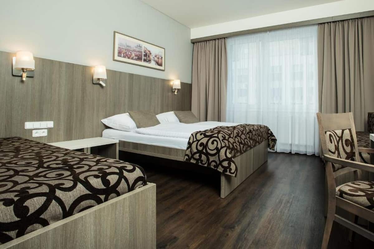 Una habitación de hotel con una cama, un escritorio, una silla y un ventanal con cortinas.